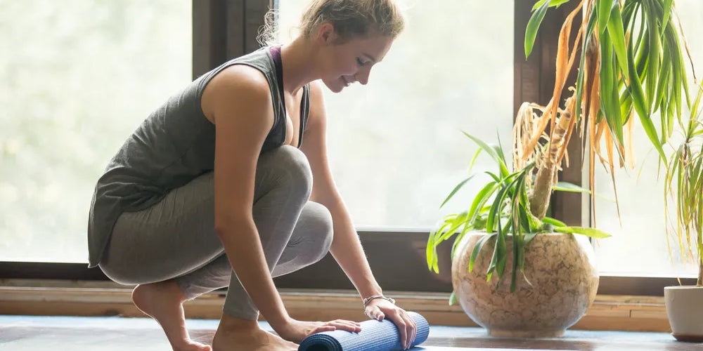 Frau rollt Yogamatte für Progressive Muskelentspannung und innere Ruhe zusammen.