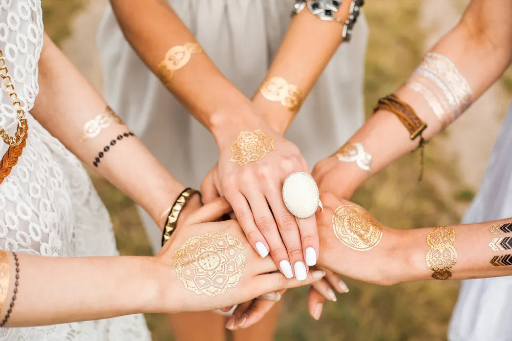 Frauenhände, die zum Schwur aufeinander liegen mit goldenen Tattoos, symbolisieren Einheit und Verbundenheit.