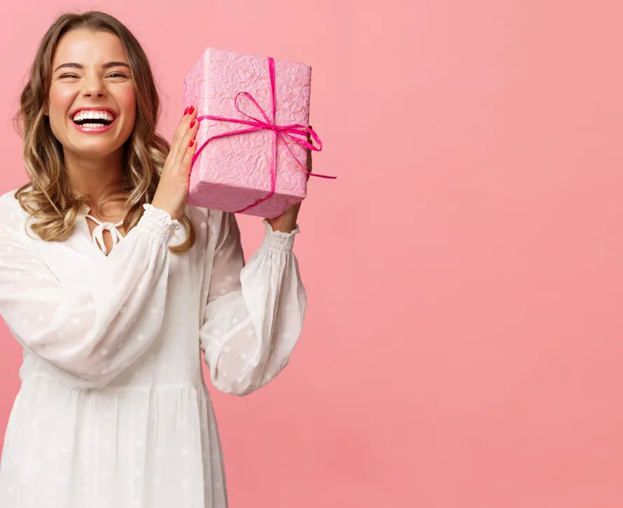 Lachende Frau hält pinkes Geschenkpaket, symbolisiert Freude, Neuigkeiten und Rabatte vom Sera Benia Verlag.