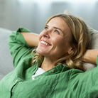 Glückliche Frau entspannt auf Sofa, symbolisiert innere Ruhe und positive Lebensveränderung durch Meditation.