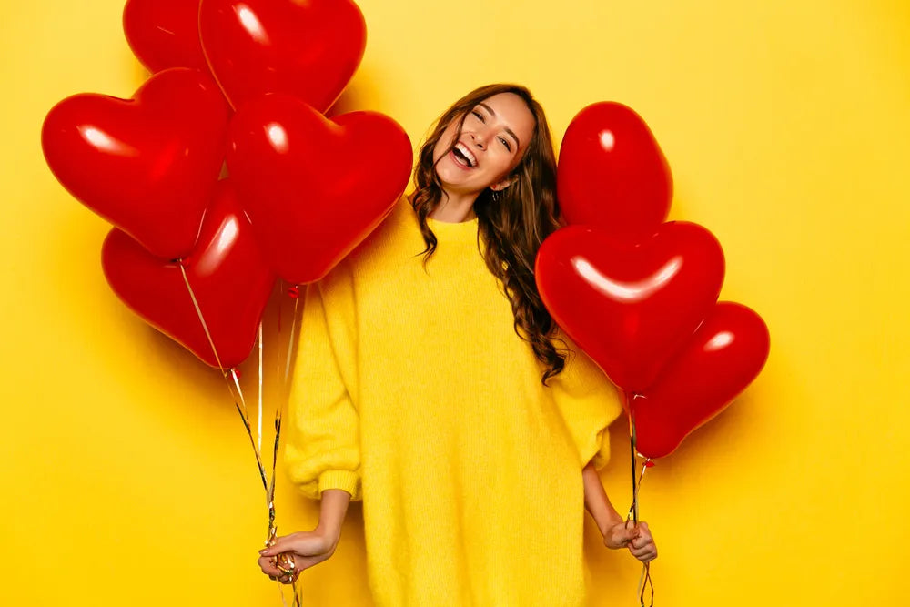 Junge Frau hält lachend große Herz-Luftballons
